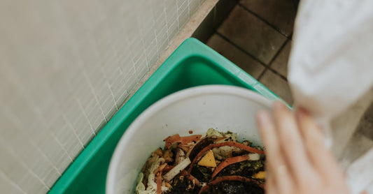 View of hands adding food scraps to a compost bin with visible soil.