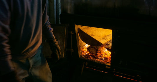 Person tending to a wood fire in a dimly lit room, adding logs to the flames.