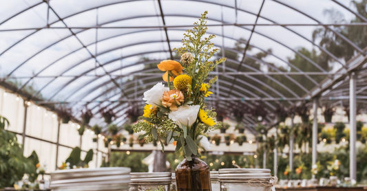 A beautifully decorated table with floral centerpieces in a sunlit greenhouse setting.