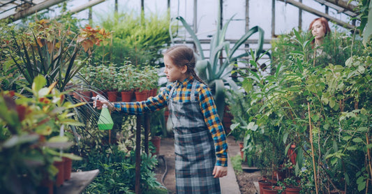 A child waters plants in a vibrant indoor greenhouse setting.