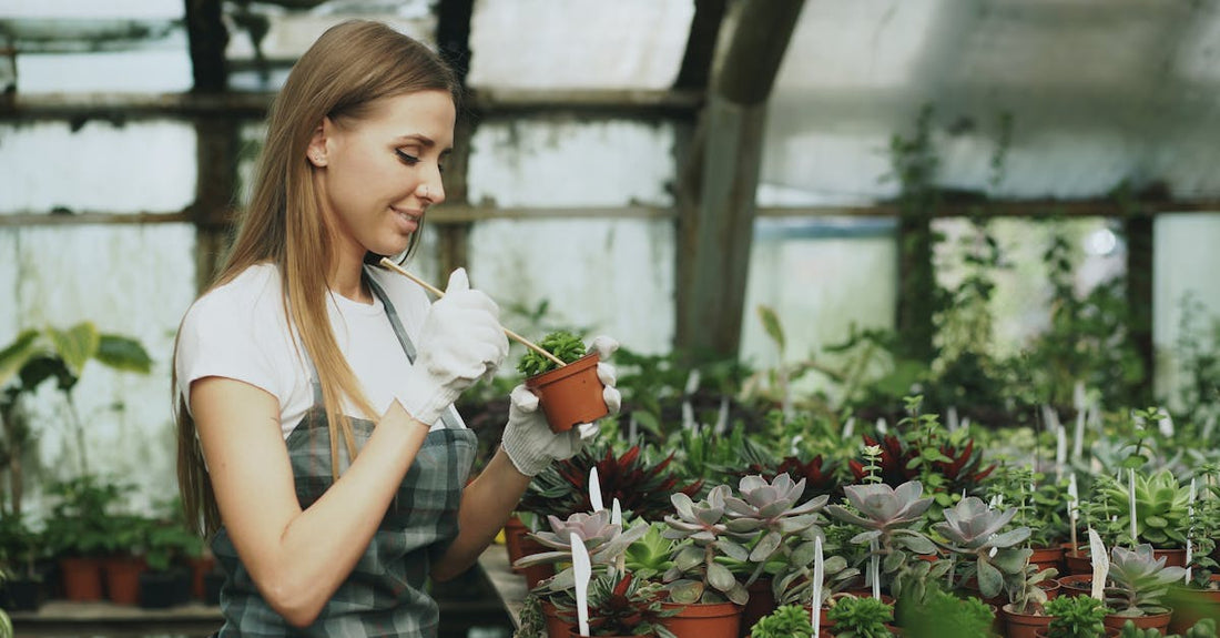 A woman tending to potted plants in a greenhouse, wearing gloves and an apron.