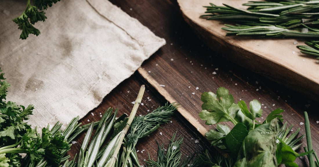 A variety of fresh herbs including rosemary, dill, and basil arranged on a wooden board for culinary use.