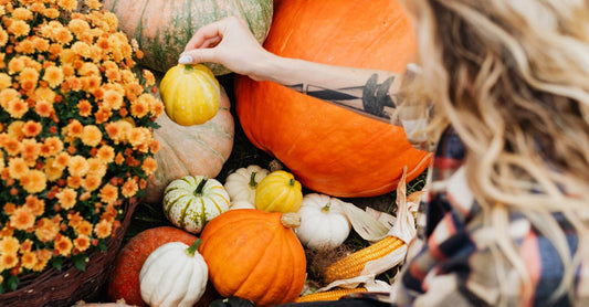 Woman arranging pumpkins and flowers in a fall garden setting.