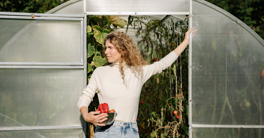 A woman standing at a greenhouse entrance holding produce, embodying autumn harvest.